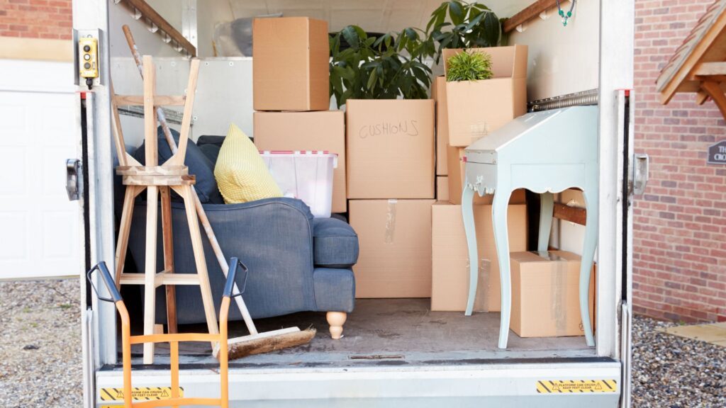 Garage rempli de cartons de déménagement, mobilier bleu, plantes vertes et équipements de rangement empilés