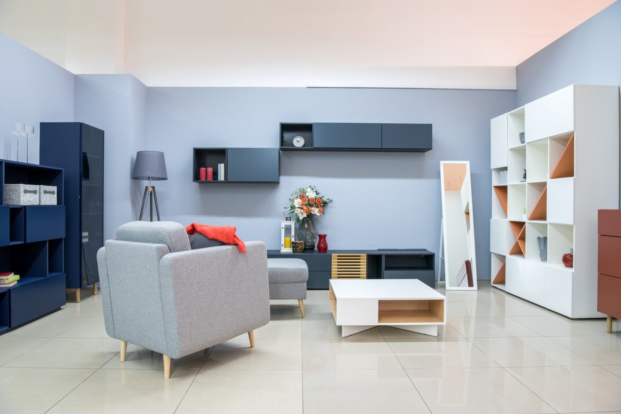Salon moderne avec fauteuil gris, canapé, table basse blanche, étagères de rangement blanc et bleu marine, murs bleu clair