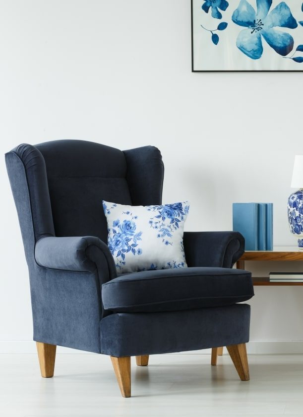 Fauteuil bleu marine vintage avec accoudoirs, orné d'un coussin bleu et blanc à motifs floraux, dans un intérieur moderne et